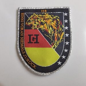 May include: A black and silver embroidered patch with a wolf's head, a German flag, and the text "EINIG VORAN NIEMALS ZUR&Uuml;CK" and "118" in orange. The patch has a silver border with stars.