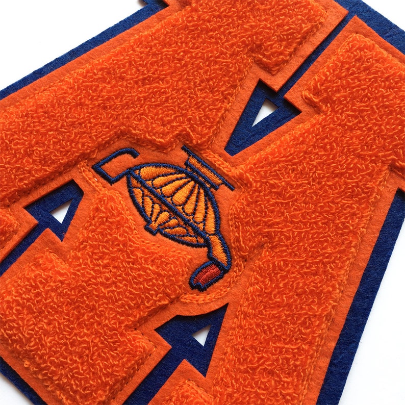 May include: Orange and blue felt letter A with a small orange and yellow embroidered design in the center.