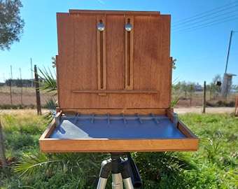May include: A wooden easel with a grey tray and a silver tripod stand. The easel is open and ready for painting.
