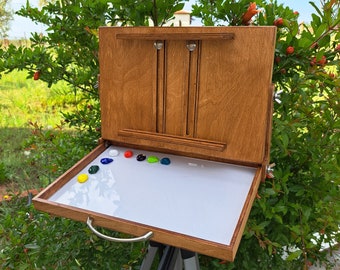 May include: A wooden easel with a white palette and a selection of colourful paints. The easel is set up on a tripod and is ready for painting.