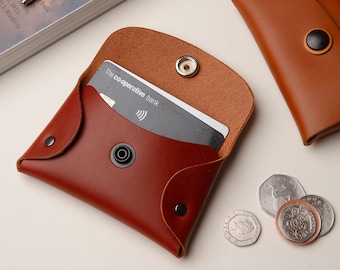 May include: Two leather wallets, one brown and one burgundy. The burgundy wallet is open and has a black card inside with the text "The co-operative bank".