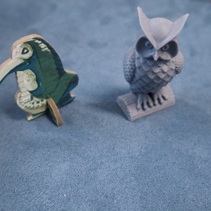May include: A green and white wooden bird figurine with a long beak and a gray owl figurine with a textured surface.