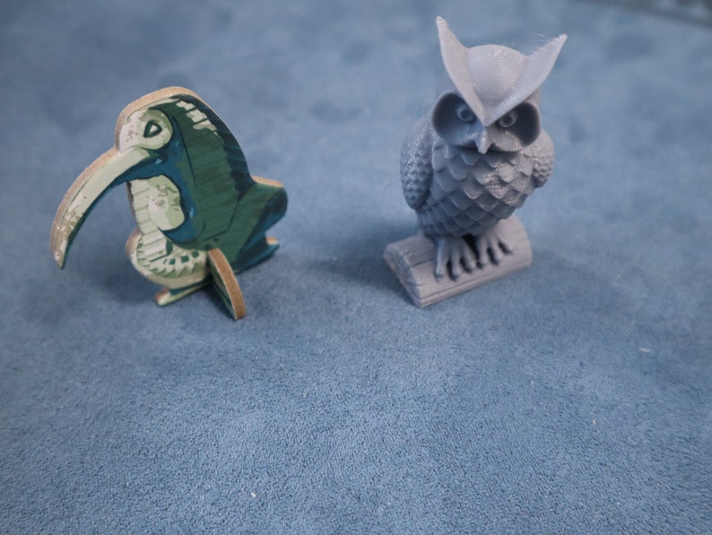 May include: A green and white wooden bird figurine with a long beak and a gray owl figurine with a textured surface.