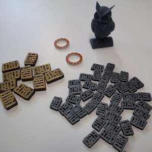 May include: A collection of small, rectangular tiles with a grid pattern. The tiles are in two colors: gold and gray. There is also a small, gray 3D printed owl figurine.
