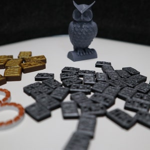May include: A gray 3D printed owl figurine, a set of brown wooden tiles, and a set of gray plastic tiles. The tiles are scattered on a white surface.