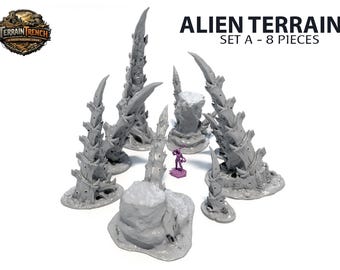 Può includere: Set di terreno alieno A, 8 pezzi. Il set include diversi elementi di terreno grigi, appuntiti e strutturati, simili a formazioni rocciose aliene. Una piccola statuina viola è posizionata tra il terreno. Viene visualizzato il testo "Alien Terrain Set A - 8 Pieces".