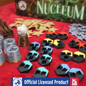 Pode incluir: Uma coleção de peças de jogo impressas em 3D para o jogo de tabuleiro Nucleus. As peças são de várias cores, incluindo cinza, marrom, azul, vermelho e amarelo. As peças são feitas de plástico e têm uma superfície texturizada. As peças de jogo estão dispostas sobre uma superfície de feltro vermelho. A caixa do jogo é visível no fundo.