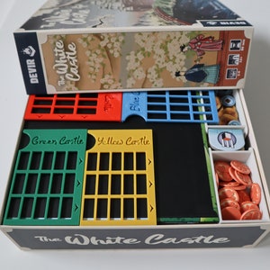 May include: A game box organizer for The White Castle board game. The organizer has compartments for the game's components, including the game board, cards, and tokens. The organizer is made of cardboard and has a white finish.