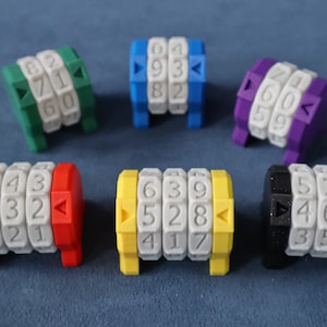 Puede incluir: Seis cerraduras de combinación de tres dígitos de colores diferentes con números blancos. Las cerraduras están dispuestas en círculo sobre una superficie azul.