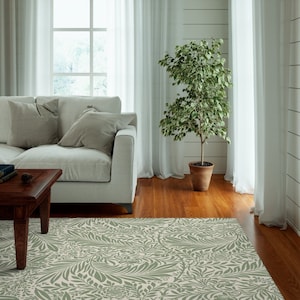 May include: A green and white patterned area rug with a floral design. The rug is in a living room with a white sofa, a coffee table, and a potted plant.