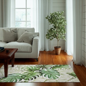 May include: A white living room with a white couch, a wooden coffee table, and a green plant in a brown pot. A white rug with a green tropical leaf pattern is on the floor.