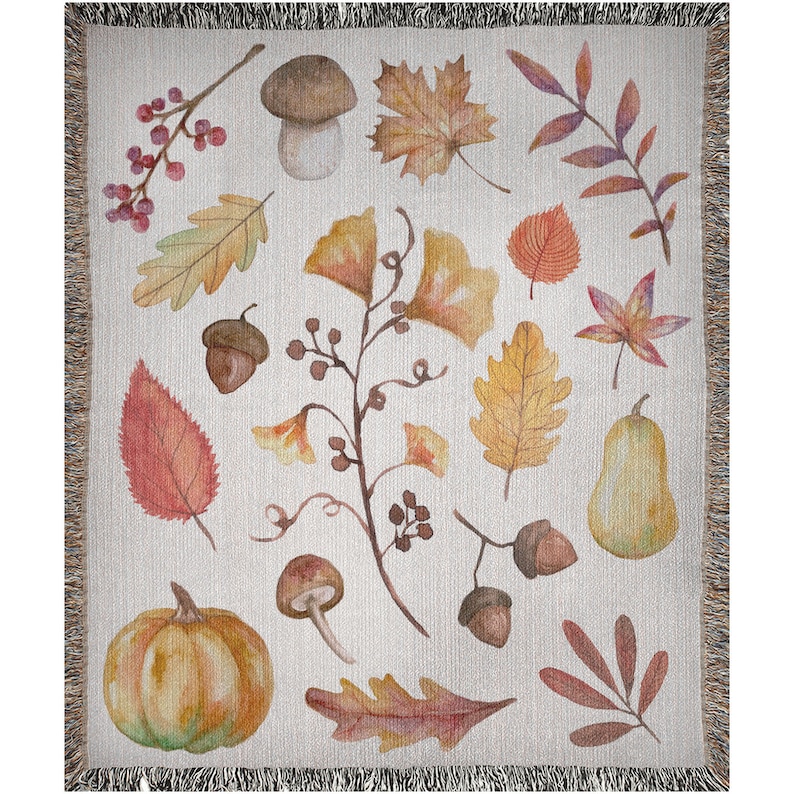 May include: Woven throw blanket featuring a watercolor design of autumn leaves, acorns, mushrooms, and a pumpkin. The blanket has a cream-colored background with a fringed edge. The artwork includes shades of orange, yellow, and brown.