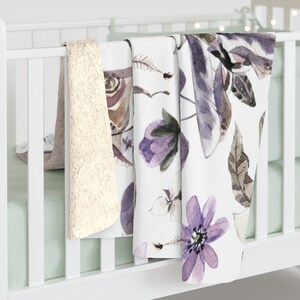 May include: Three baby blankets, one white with a purple floral and butterfly pattern, one white with a brown butterfly pattern, and one beige fuzzy blanket.