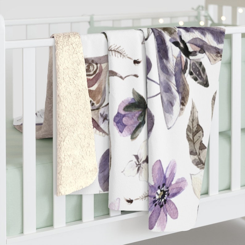 May include: Three baby blankets, one white with a purple floral and butterfly pattern, one white with a brown butterfly pattern, and one beige fuzzy blanket.