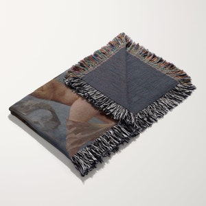May include: A woven throw blanket with a colourful fringe border. The blanket features a printed design of a painting of a nude figure.