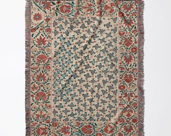 Peut inclure: Un plaid tissé présentant un fond crème avec un panneau central composé de petits motifs floraux répétitifs bleus et rouges. La bordure affiche un motif plus grand et complexe de fleurs rouges et de feuillage vert avec des franges.
