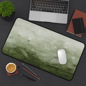 Peut inclure: Un tapis de souris de bureau en aquarelle verte avec une souris d'ordinateur blanche sur le dessus. Le tapis est sur une surface noire avec un ordinateur portable, une tasse de café, des crayons et un stylo.