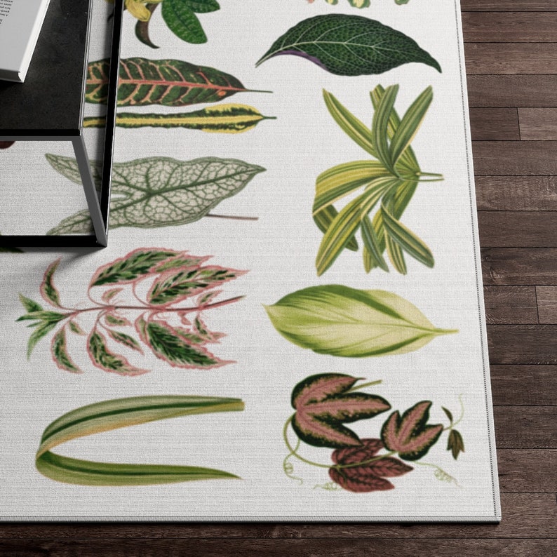 May include: A white rug with a botanical print featuring various green and pink leaves. The leaves are arranged in a repeating pattern and are outlined in black.