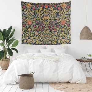 May include: A rectangular wall tapestry featuring a dense, symmetrical botanical pattern with stylized flowers and foliage in shades of deep navy blue, golden yellow, and muted coral pink, displayed flat against a wall above a white bed.