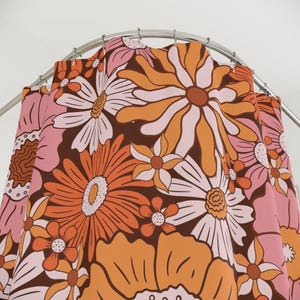 a vibrant, colorful floral pattern with a mix of orange, pink, and white flowers. The pattern is displayed on a shower curtain, which is hanging from a rod. The shower curtain appears to be a decorative piece, adding a touch of color and style to the bathroom.