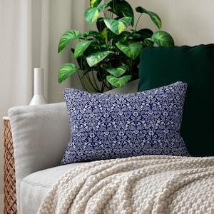 May include: A navy blue throw pillow with a white floral pattern. The pillow is sitting on a light gray couch with a white throw blanket.