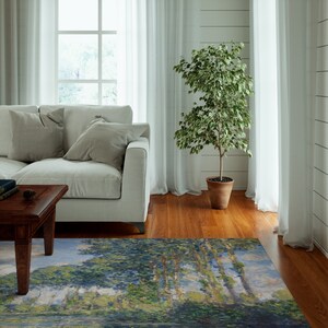May include: A light blue, green, and white area rug with a painting of trees and a river. The rug is in a living room with a white couch, a coffee table, and a potted plant.