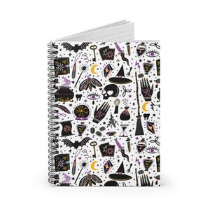 May include: A white spiral notebook with a black and white pattern of witchy symbols, including a cauldron, a skull, a broom, a crystal ball, a wand, a bat, a crescent moon, a hand, a key, a potion bottle, and a witch's hat. The pattern is repeated throughout the notebook.