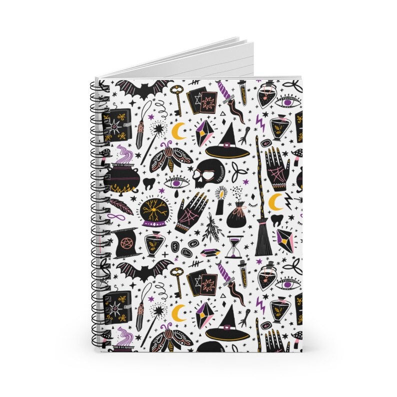 May include: A white spiral notebook with a black and white pattern of witchy symbols, including a cauldron, a skull, a broom, a crystal ball, a wand, a bat, a crescent moon, a hand, a key, a potion bottle, and a witch's hat. The pattern is repeated throughout the notebook.