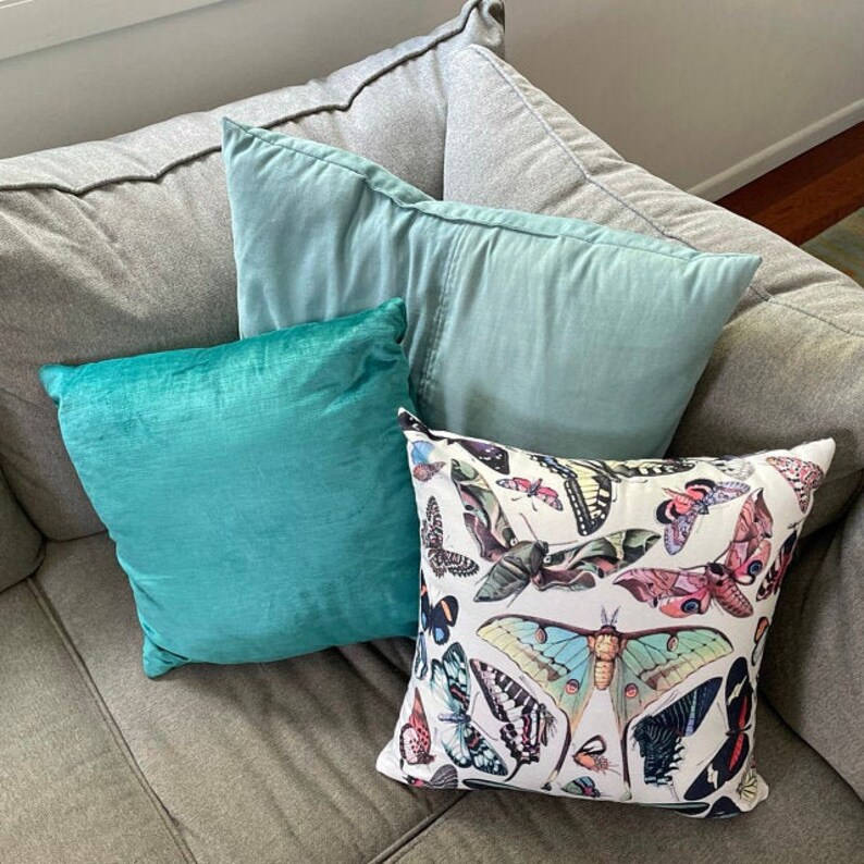 May include: A gray couch with three throw pillows. The pillows are teal, light blue, and white with a butterfly pattern.