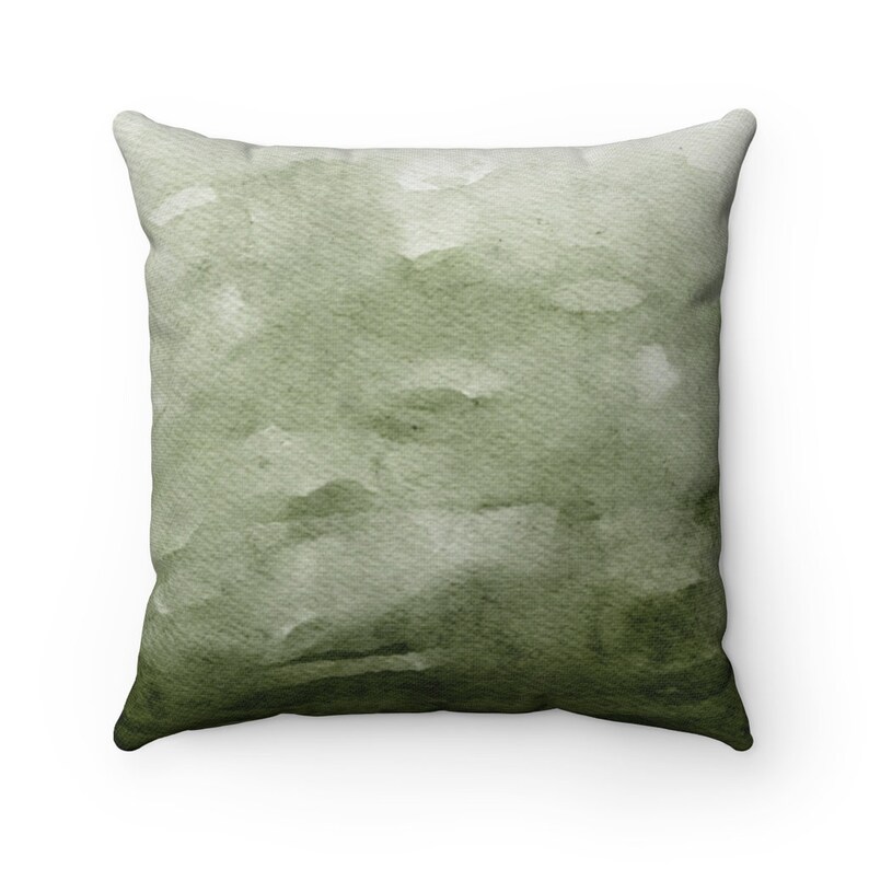 May include: A green watercolor throw pillow with a faded, abstract design. The pillow is square and has a soft, plush texture.