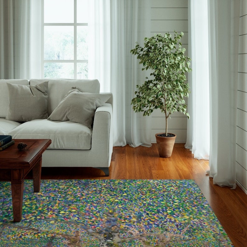 May include: A colorful abstract area rug with a blue, green, and yellow color scheme. The rug is in a living room setting with a white couch and a potted plant.