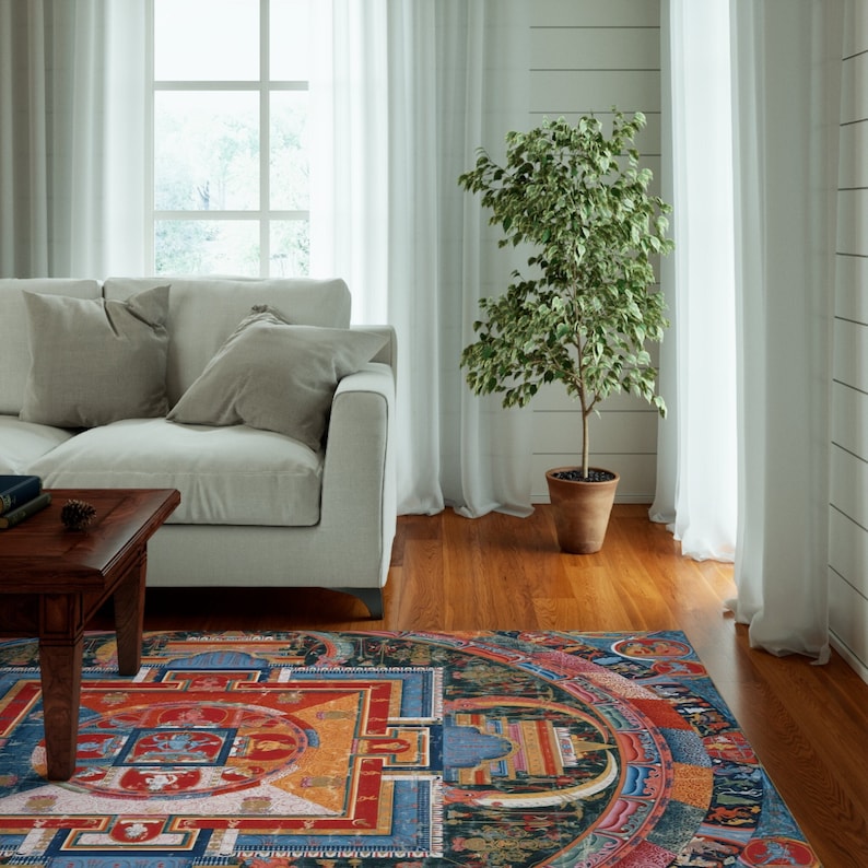 May include: A colorful mandala rug with intricate details in shades of blue, red, yellow, and green. The rug is laid out on a hardwood floor in a living room setting with a white couch and a potted plant.