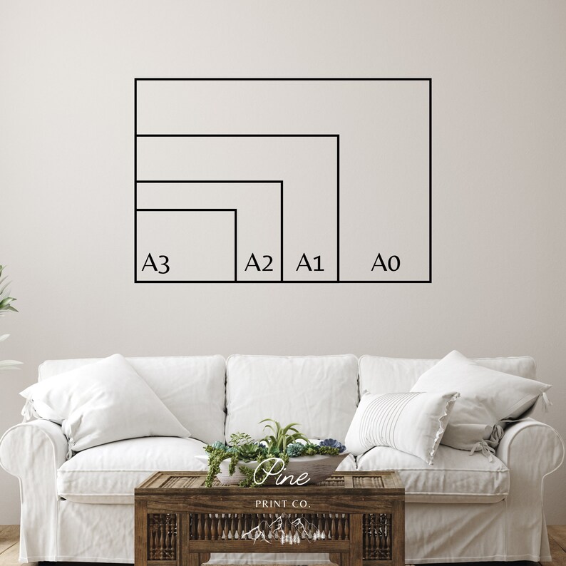 May include: A white wall with a black outline of four different sizes of paper, labeled A0, A1, A2, and A3. The paper sizes are displayed in descending order from largest to smallest. The wall is behind a white couch with a wooden coffee table in front of it.