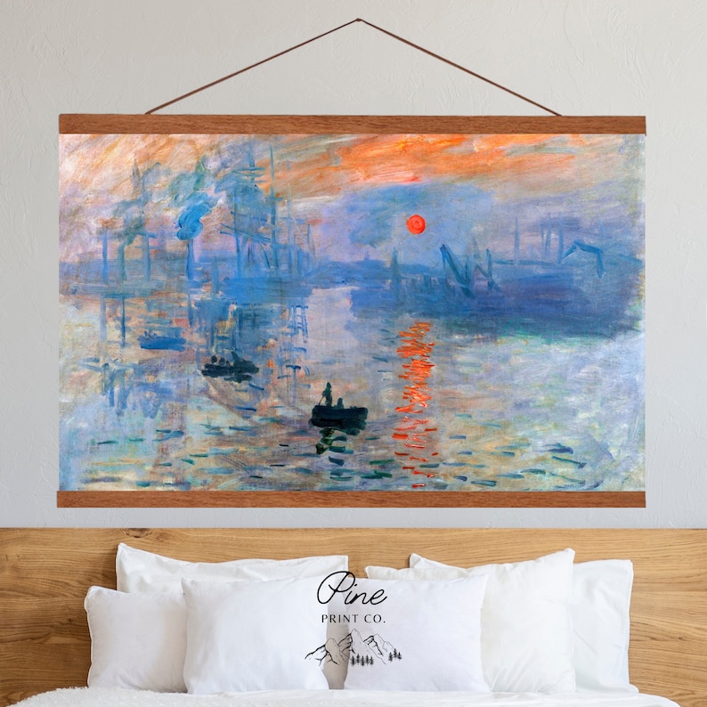May include: A canvas print of Claude Monet's Impression, Sunrise, depicting a hazy sunrise over a harbor with ships and a small boat in the foreground. The print is framed with a wooden frame and hanging on a wall above a bed with white pillows.