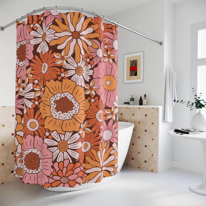 a bathroom with a shower curtain adorned with a vibrant floral pattern in shades of orange, pink, and white. The shower curtain is hanging from a rod, and the bathroom has a white sink and a white table with a plant on it.