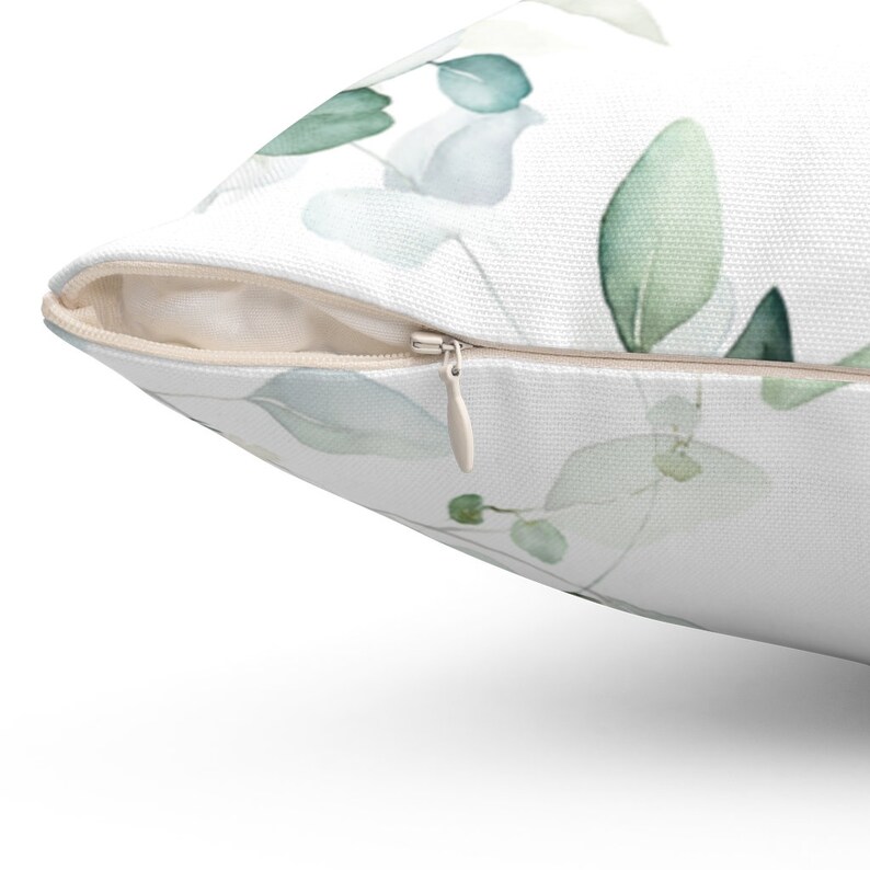 May include: A white pillow with a zipper closure. The pillow has a watercolor design of green and blue leaves.