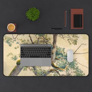 May include: A desk mat with a watercolor painting of a tree with green leaves and brown branches on a beige background. A laptop computer and a white mouse are on the desk mat.