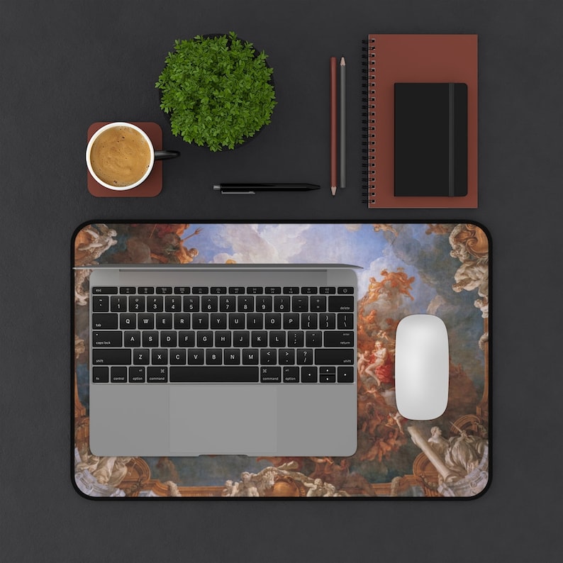 May include: A black and white laptop computer with a keyboard and trackpad is on a desk mat with a colorful painting of a sky with clouds and angels. A white mouse is on the desk mat. There is a potted plant, a cup of coffee, two pencils, and a pen on the desk.