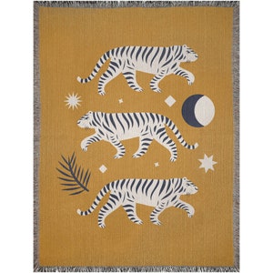 May include: A mustard yellow woven throw blanket with a repeating pattern of three white tigers with black stripes walking across a field of stars and a crescent moon.