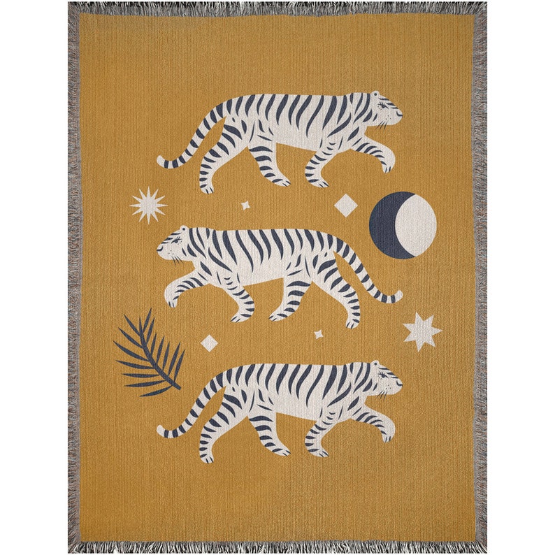 May include: A mustard yellow woven throw blanket with a repeating pattern of three white tigers with black stripes walking across a field of stars and a crescent moon.