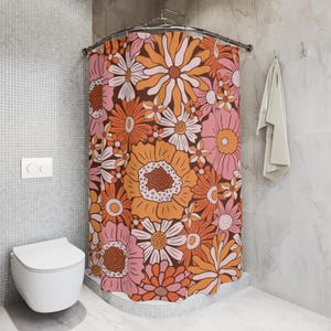 a bathroom with a shower curtain adorned with a vibrant floral pattern in shades of orange, pink, and white. The shower curtain is hanging from a rod next to a white towel. The bathroom also includes a toilet and a tiled wall.