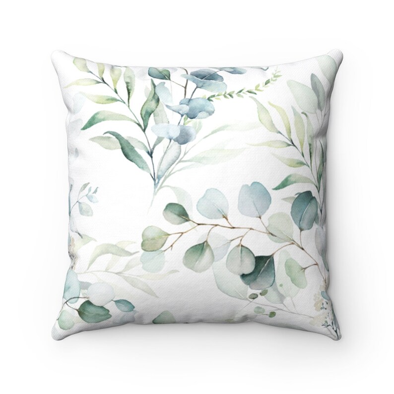 May include: A white throw pillow with a watercolor design of green and blue leaves and flowers.