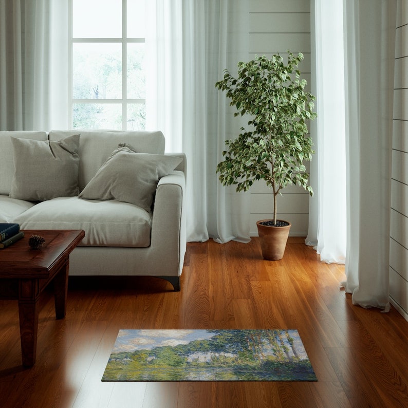 May include: A rectangular rug with a painting of a river scene with trees and a cloudy sky. The rug is on a hardwood floor in a living room setting.