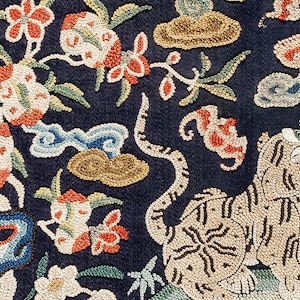 Puede incluir: Primer plano de una tela azul oscuro con bordado intrincado. El dise&ntilde;o presenta un tigre, flores y nubes, todo creado con cuentas y hilos de colores.
