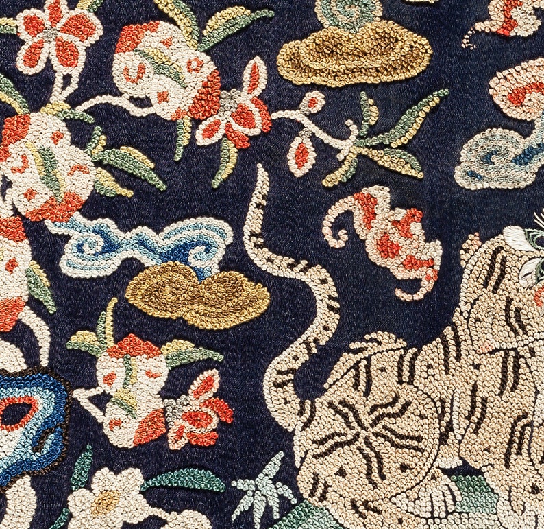 Puede incluir: Primer plano de una tela azul oscuro con bordado intrincado. El dise&ntilde;o presenta un tigre, flores y nubes, todo creado con cuentas y hilos de colores.
