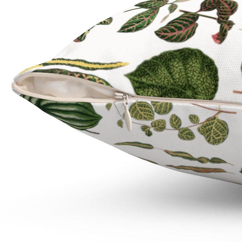 May include: A white throw pillow with a zipper closure features a repeating pattern of green and red leaves. The pillow is made of a soft, comfortable fabric.