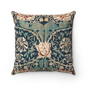 Pode incluir: Uma almofada quadrada com fundo azul e um padr&atilde;o floral em tons de branco, verde e laranja. O padr&atilde;o apresenta flores e folhas estilizadas.