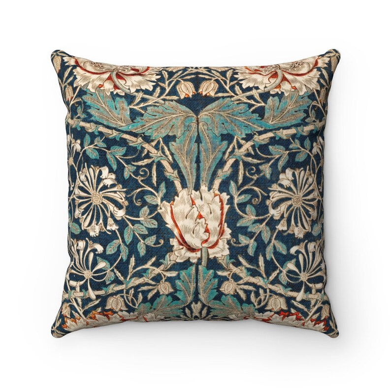 Pode incluir: Uma almofada quadrada com fundo azul e um padr&atilde;o floral em tons de branco, verde e laranja. O padr&atilde;o apresenta flores e folhas estilizadas.
