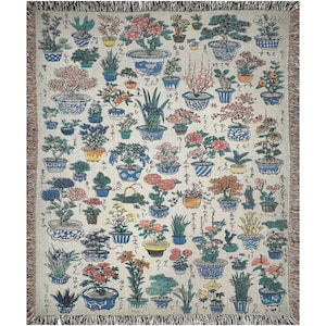 May include: A woven tapestry throw blanket featuring a repeating pattern of potted plants and flowers in various colors, including pink, red, blue, green, and yellow. The background is a cream color with Japanese characters.