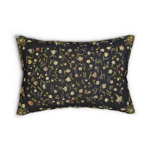 Puede incluir: Una almohada negra con un patr&oacute;n floral que presenta una variedad de flores en tonos de rosa, blanco y amarillo. Las flores est&aacute;n dispuestas en un patr&oacute;n aleatorio sobre un fondo oscuro.